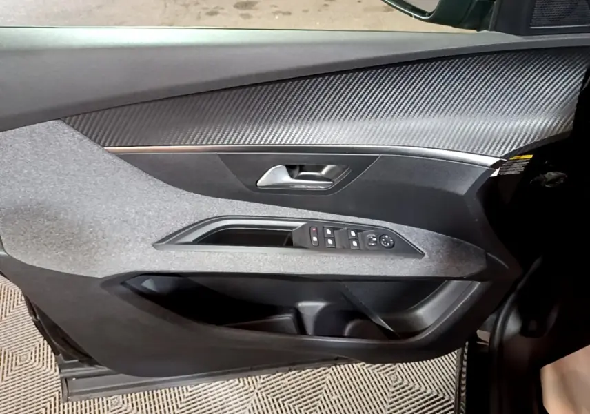 Gros plan sur la porte avant gauche noire du Peugeot 5008 2021, avec commandes des vitres et insert effet carbone.