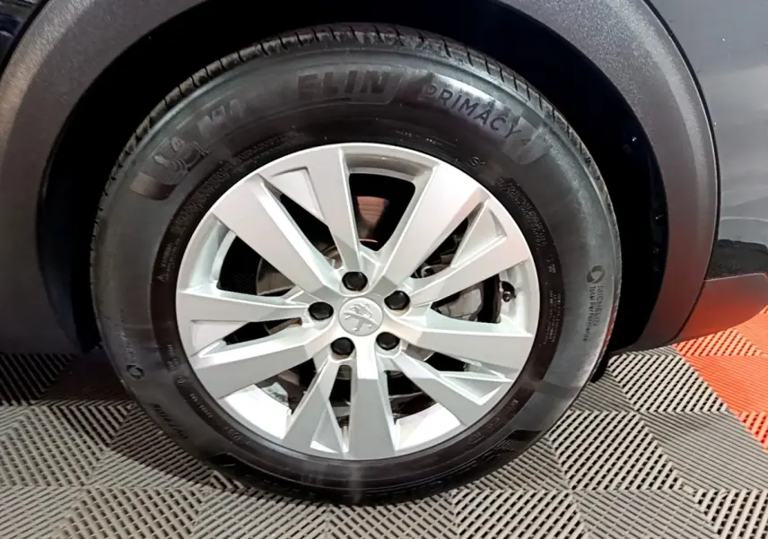 Gros plan sur la roue avant droite d’un Peugeot 5008 noir, mettant en valeur la jante argentée et le pneu Michelin.