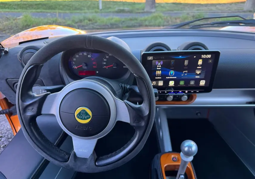 Vue intérieure centrée sur le volant cuir noir et le tableau de bord avec écran tactile de la Lotus Elise 3 Cup 250 orange.