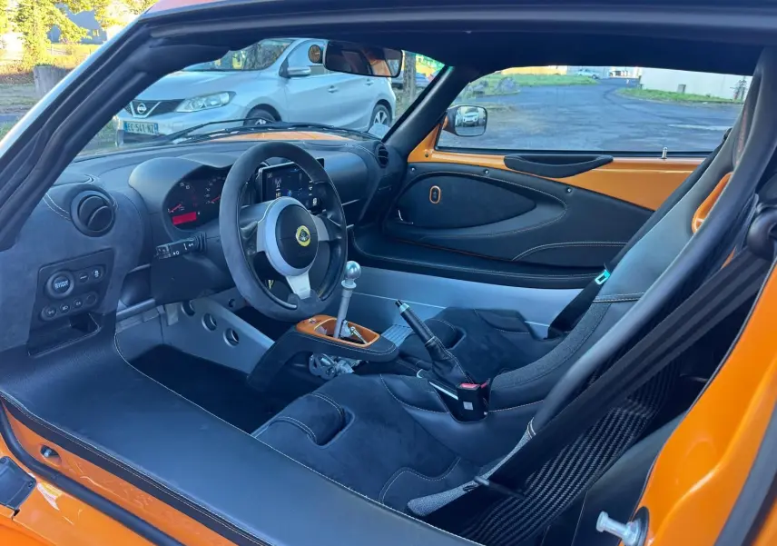 Vue intérieure côté conducteur de la Lotus Elise 3 Cup 250 orange, avec sièges sport en Alcantara noir et volant cuir.