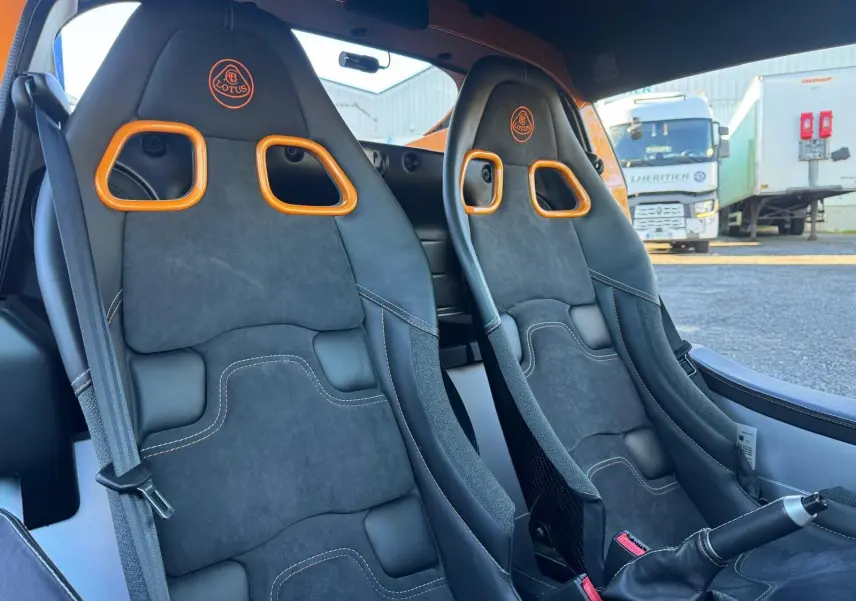 Vue intérieure rapprochée des sièges sport noirs avec surpiqûres orange et harnais de la Lotus Elise 3 Cup 250 2021.