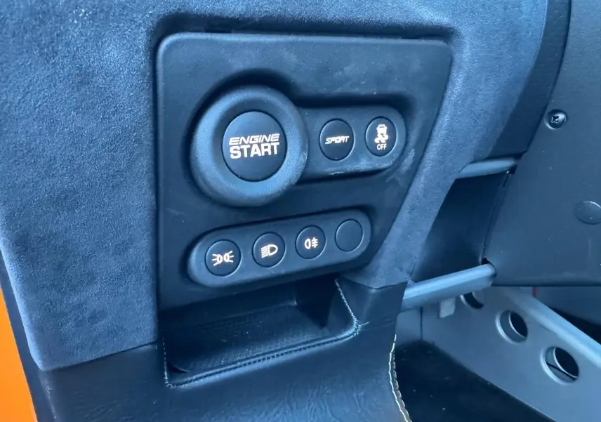 Gros plan sur le tableau de bord côté conducteur de la Lotus Elise 3 Cup 250 orange, avec bouton démarrage moteur et commandes.