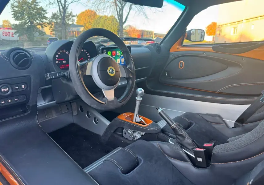 Intérieur côté conducteur de la Lotus Elise 3 Cup 250 orange, volant cuir noir et levier de vitesses aluminium poli.