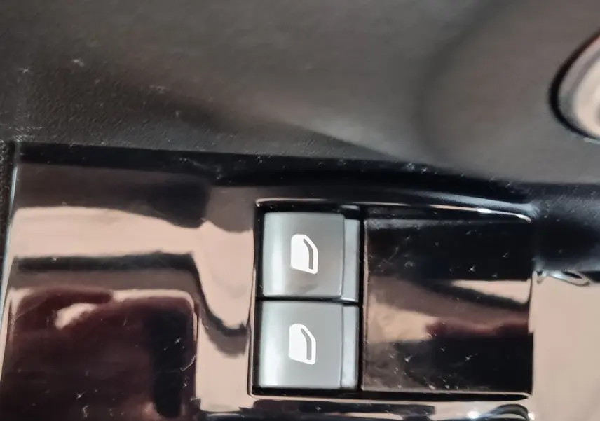 Gros plan sur les boutons de commande des vitres électriques côté conducteur d'une Citroën C3 blanche.