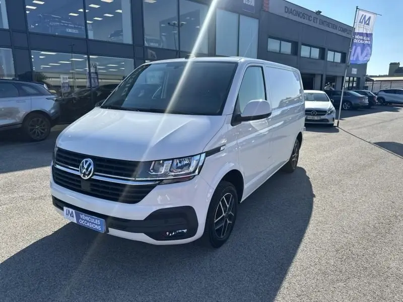 Vue 3/4 avant droite d'un Volkswagen Transporter blanc 2022 avec jantes noires, stationné devant un garage.