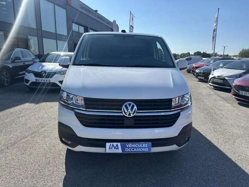 Vue frontale d'un Volkswagen Transporter blanc 2022 avec calandre noire et logo VW bien visible, sur parking extérieur.