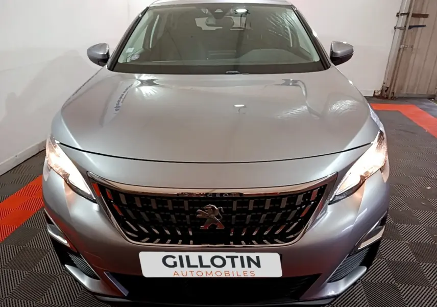 Vue avant d’un Peugeot 3008 gris clair avec calandre noire et phares allumés dans un garage.