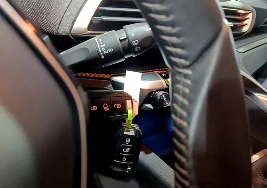 Gros plan intérieur côté conducteur du Peugeot 3008 gris clair, volant cuir et commandes de phares visibles.