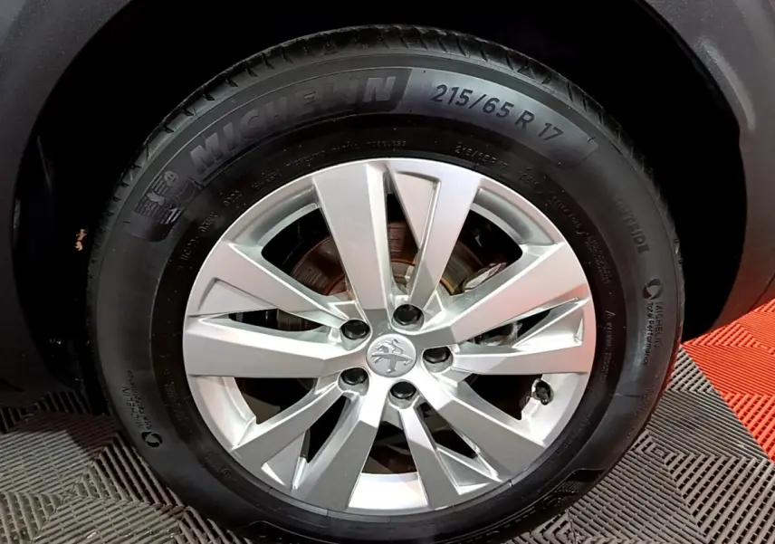 Gros plan sur la roue avant droite d’un Peugeot 3008 gris clair, jante alliage argent avec pneu Michelin.