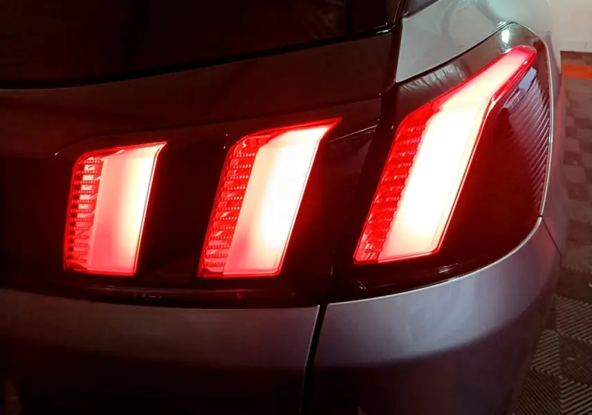 Gros plan sur les feux arrière allumés côté gauche d’un Peugeot 3008 gris clair, version 2020.