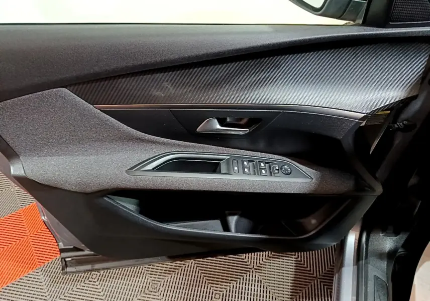 Vue rapprochée de la porte avant gauche grise du Peugeot 3008 avec commandes électriques et insert effet carbone.