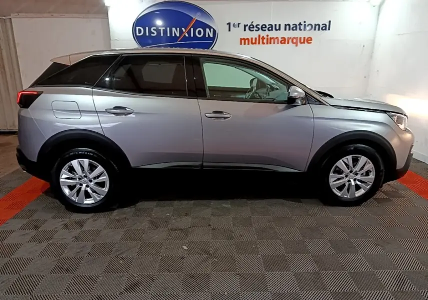 Vue de profil droit d’un Peugeot 3008 gris clair 2020 dans un showroom avec logo Distinxion en arrière-plan.