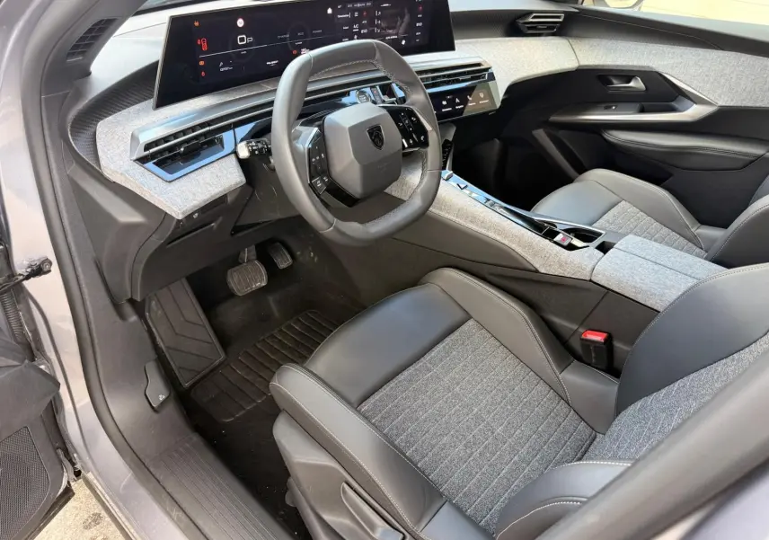 Vue intérieure côté conducteur du Peugeot 5008 Hybrid 145 en gris Artense, avec tableau de bord numérique et sellerie mixte tissu-cuir gris.