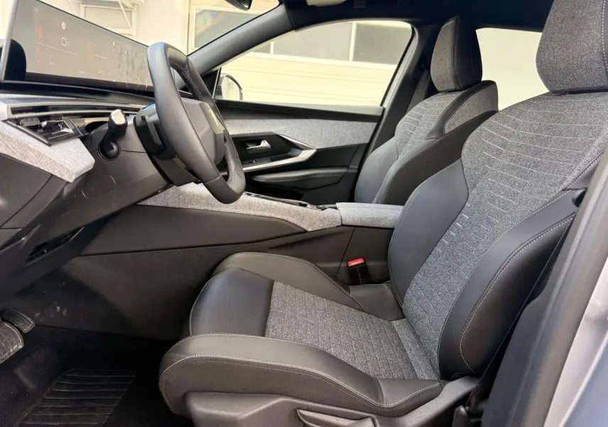 Vue intérieure côté conducteur du Peugeot 5008 Hybrid 145 en gris Artense, sièges tissu et cuir bicolores avec tableau de bord numérique.