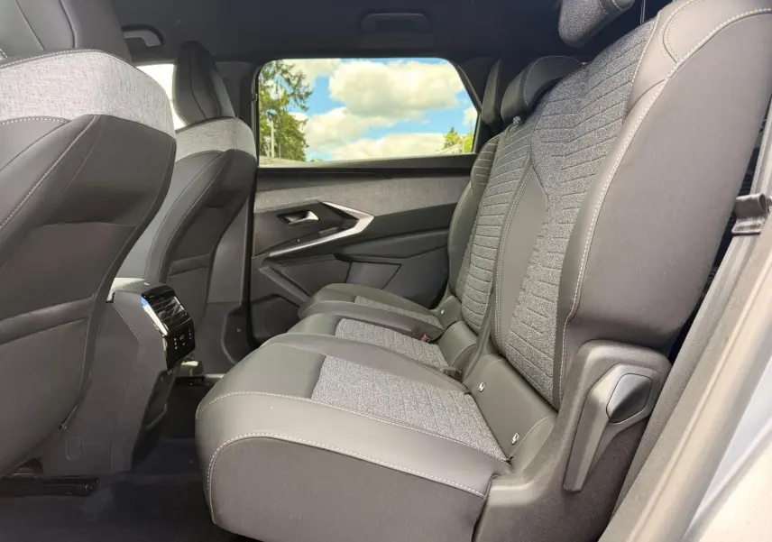 Vue latérale droite de la banquette arrière en tissu gris et cuir noir du Peugeot 5008 Hybrid 2025 avec fenêtre et ciel visible.