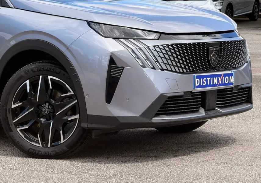 Vue avant droite du Peugeot 5008 gris Artense 2025, avec calandre noire distinctive et jante alliage bicolore.