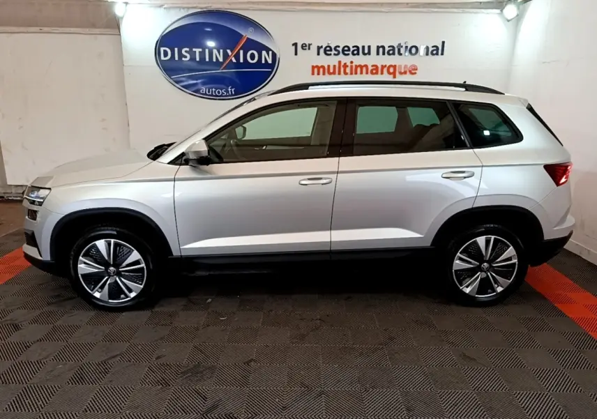 Vue latérale droite d'un Skoda Karoq gris clair 2022, avec jantes alliage et toit noir, en intérieur showroom.