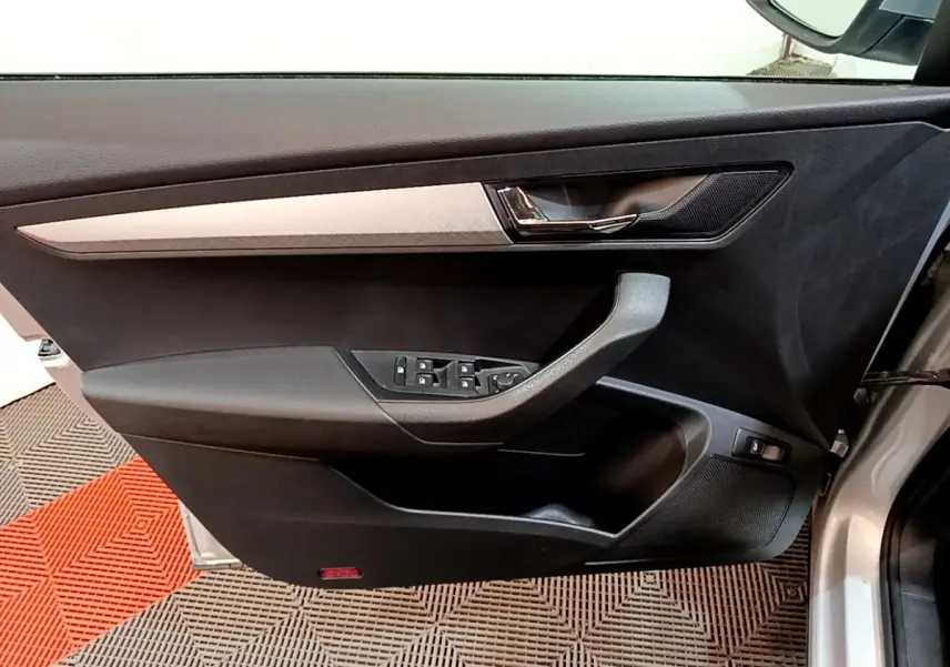 Vue intérieure côté gauche de la porte avant gris clair du Skoda Karoq avec commandes des vitres et poignée intégrée.