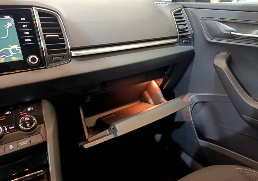 Vue intérieure côté passager du tableau de bord gris foncé d’un Skoda Karoq 2022 avec boîte à gants ouverte et éclairage intérieur.