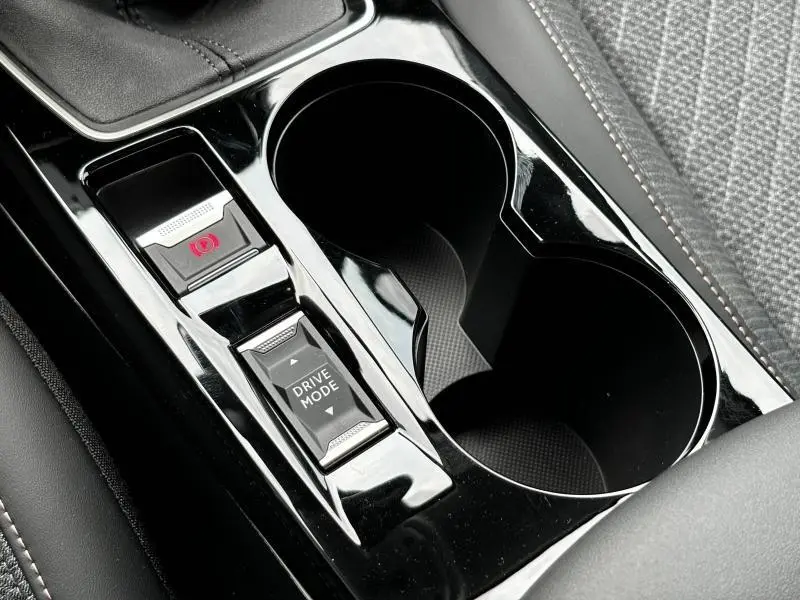 Gros plan sur la console centrale noire brillante de la Peugeot 208 2024 avec bouton Drive Mode et frein à main électrique.