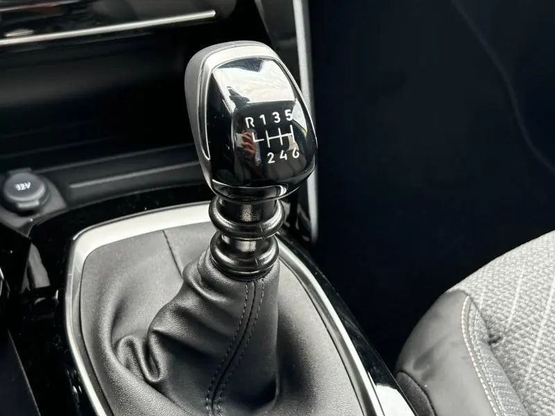 Le levier de vitesses manuel noir brillant de la Peugeot 208 1.2 PureTech, entouré de cuir et tissu gris.