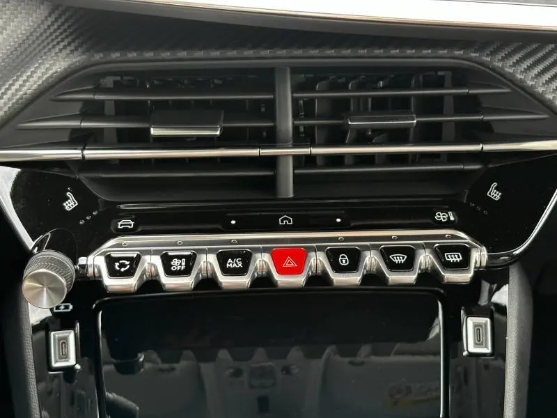 Vue rapprochée de la console centrale noire brillante du Peugeot 208 2024 avec boutons chrome et alarme rouge au centre.
