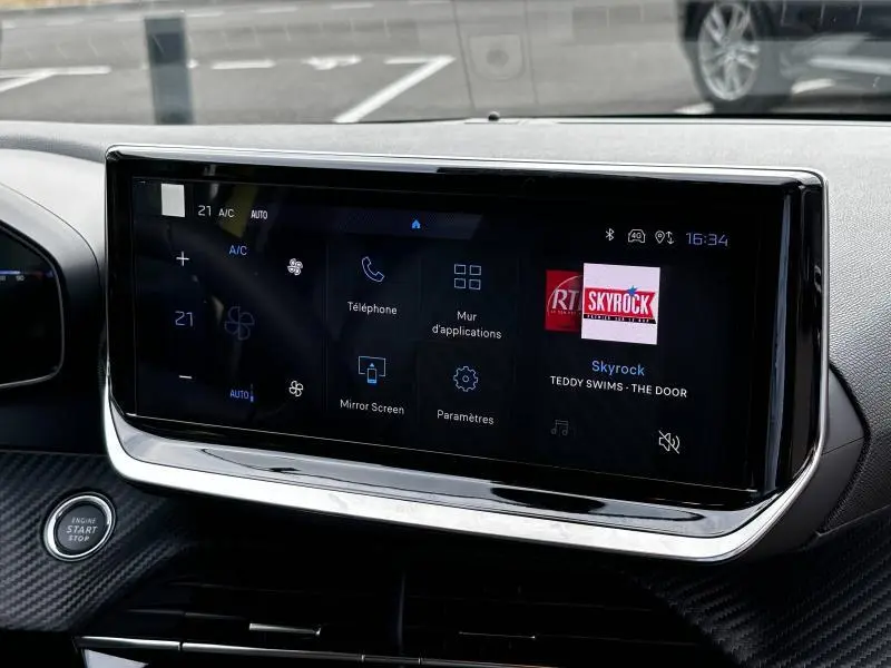 Écran tactile central allumé dans l’habitacle d’une Peugeot 208 jaune Agueda, avec commandes multimédia visibles.