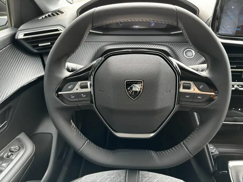 Vue frontale du volant cuir noir du Peugeot 208 2024 avec commandes intégrées et tableau de bord texturé gris.