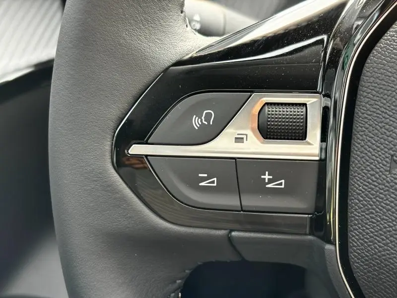 Gros plan sur les commandes audio au volant noir brillant du Peugeot 208 2024, avec molette et boutons de volume.
