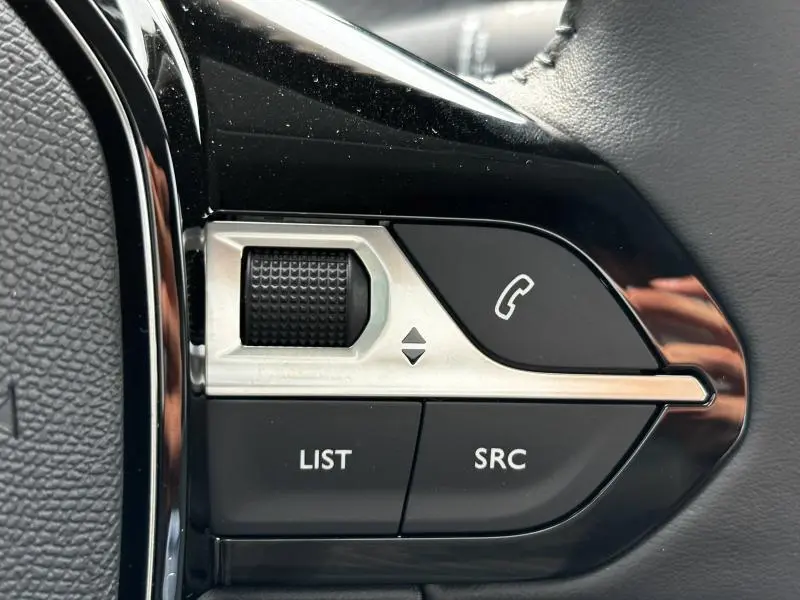 Gros plan sur les commandes noires et argentées du volant du Peugeot 208 2024, avec bouton appel et molette de défilement.