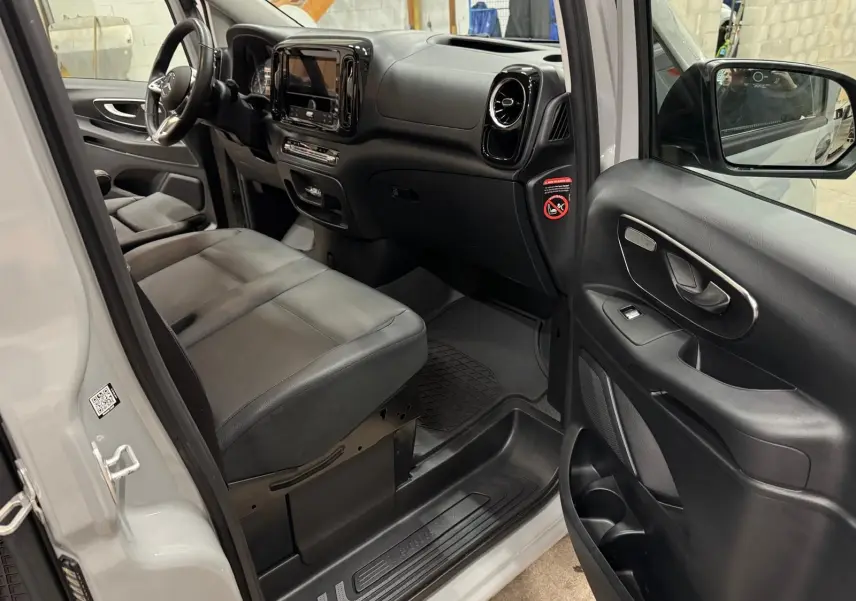 Vue intérieure côté conducteur du Mercedes Vito Mixto gris alpin, montrant sièges cuir noirs et tableau de bord moderne.
