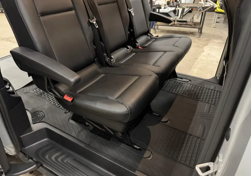 Vue intérieure côté droit sur la banquette noire 3 places en cuir avec tapis de sol caoutchouc dans un Mercedes Vito Mixto gris.
