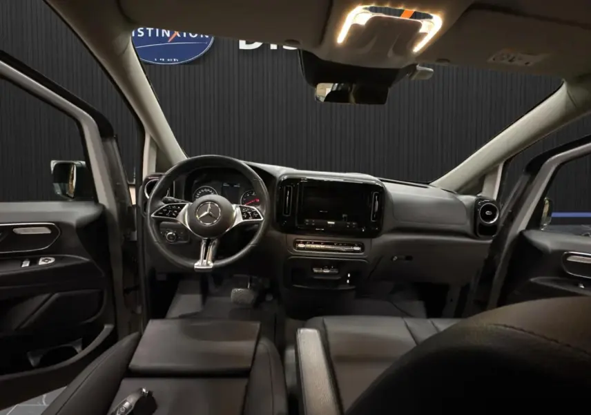 Vue intérieure avant du Mercedes Vito Mixto 2025, tableau de bord noir avec volant multifonction et écran central éteint.