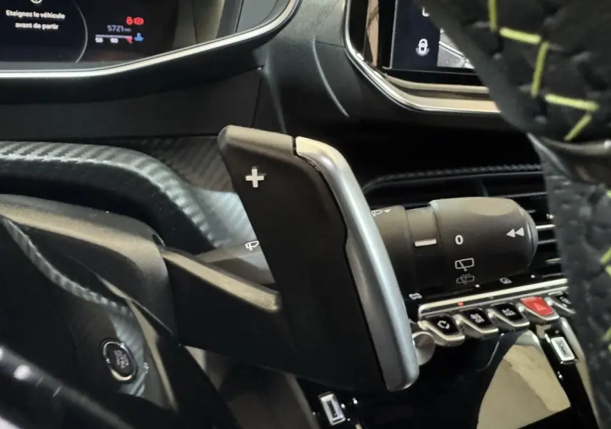 Gros plan sur la palette de changement de vitesse + côté droit du volant cuir avec surpiqûres vertes dans un Peugeot 208 gris clair.