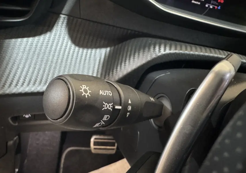 Gros plan sur la commande d’éclairage noire avec réglage automatique dans l’habitacle d’une Peugeot 208 gris clair.