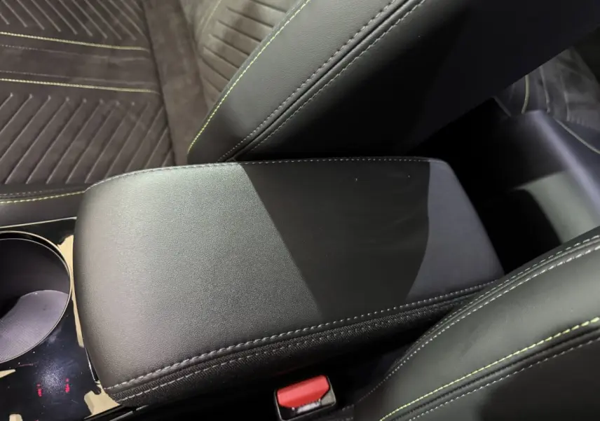 Gros plan sur l'accoudoir central en cuir noir avec surpiqûres vertes, sièges en tissu gris foncé à coutures vertes.