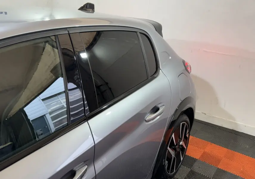 Vue côté droit arrière d'une Peugeot 208 Hybrid gris clair avec rétroviseur caméra et jante alliage noir et argent.