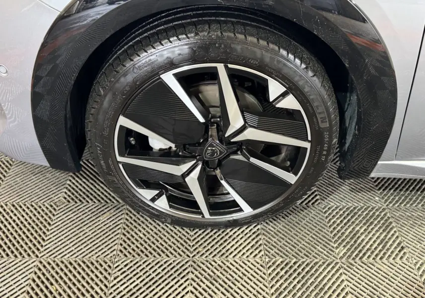 Gros plan sur la roue avant gauche de la Peugeot 208 Hybrid 136 eDCS6 GT gris clair avec jante alliage noire et argent.