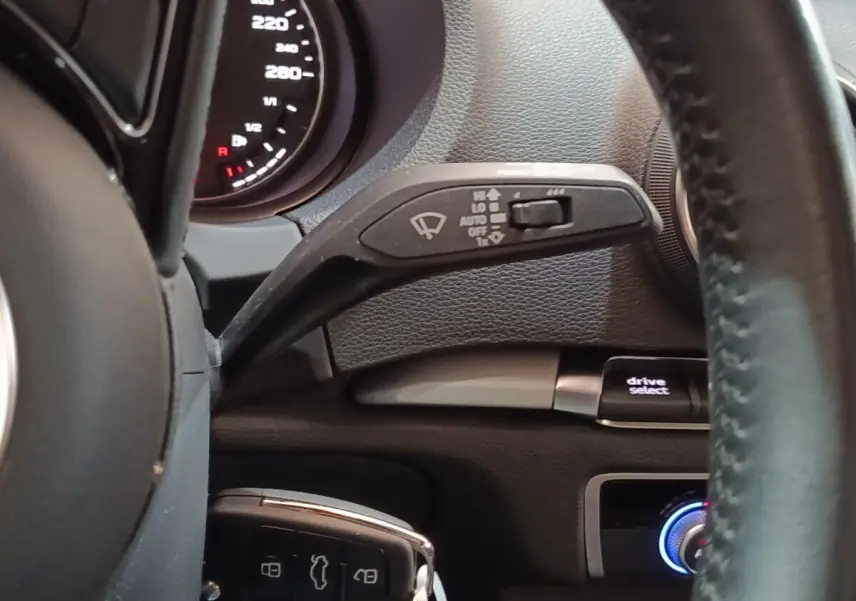 Vue rapprochée du volant cuir noir d’Audi A3 blanc 2020, avec commandes essuie-glace et bouton drive select visibles.