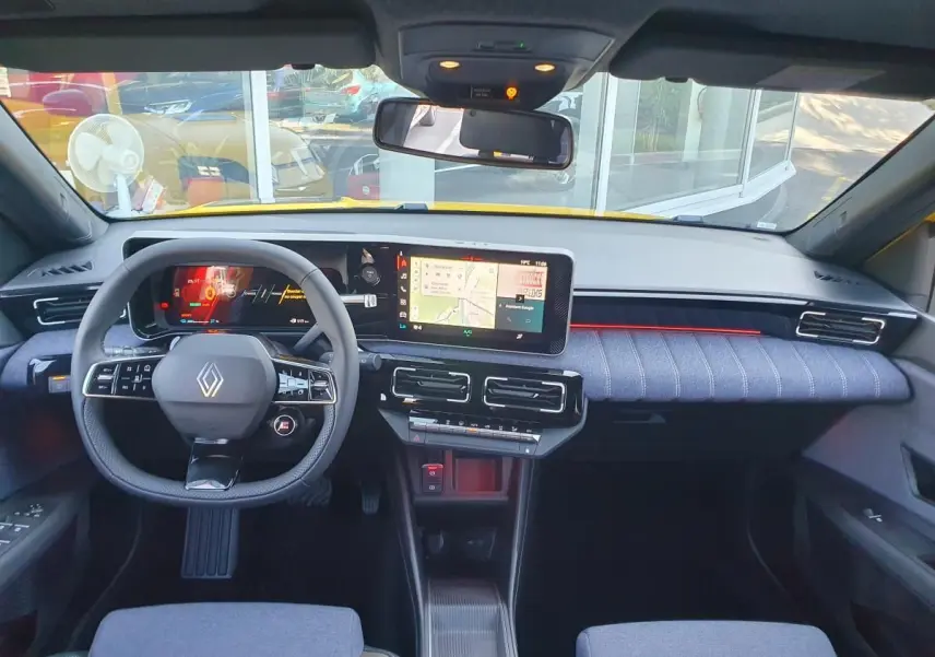 Vue intérieure avant du tableau de bord et volant de la Renault R5 E-TECH jaune avec écran tactile et éclairage d'ambiance rouge.