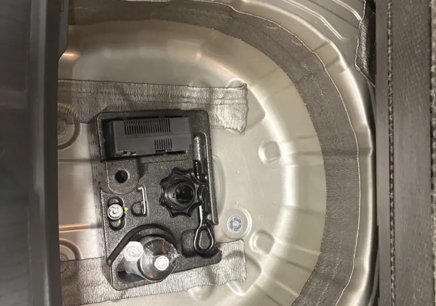 Vue rapprochée du coffre d'une Volkswagen Polo 2024 Reflet d'argent, montrant le logement de la roue de secours et l'outillage.