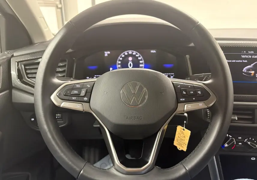 Vue rapprochée du volant multifonction noir d'une Volkswagen Polo 2024 avec tableau de bord digital allumé.