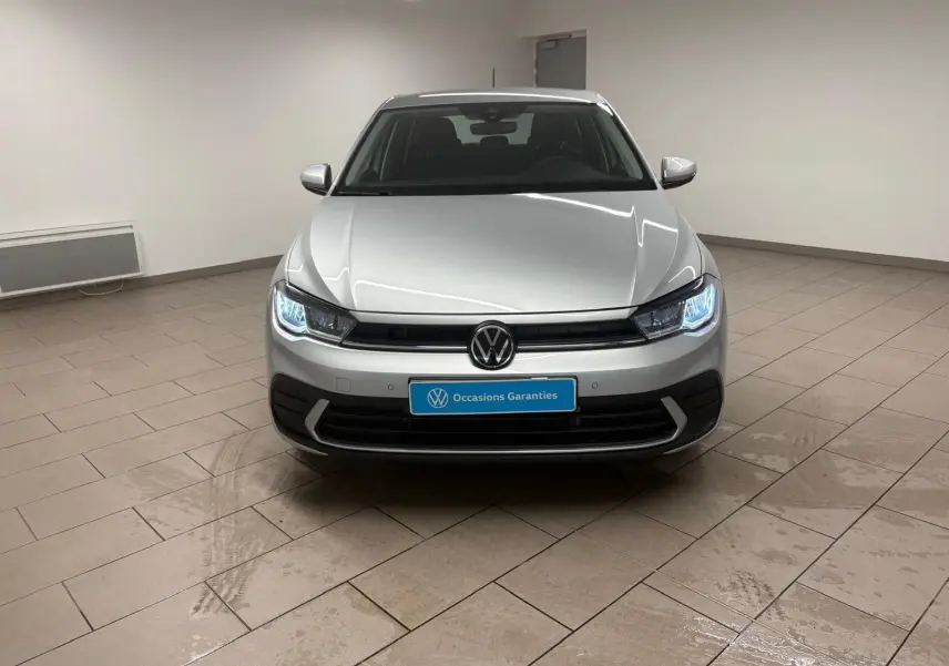 Vue frontale d'une Volkswagen Polo 2024 en peinture métallisée reflet d'argent avec phares allumés dans un showroom.