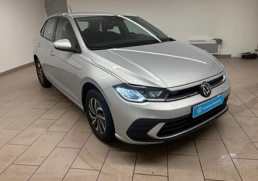 Volkswagen Polo 2024 Reflet d'argent vue 3/4 avant droit avec phares allumés en intérieur showroom.