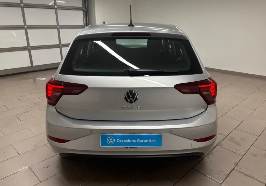 Vue arrière d'une Volkswagen Polo 2024 en peinture métallisée Reflet d'argent avec feux arrière allumés dans un garage.