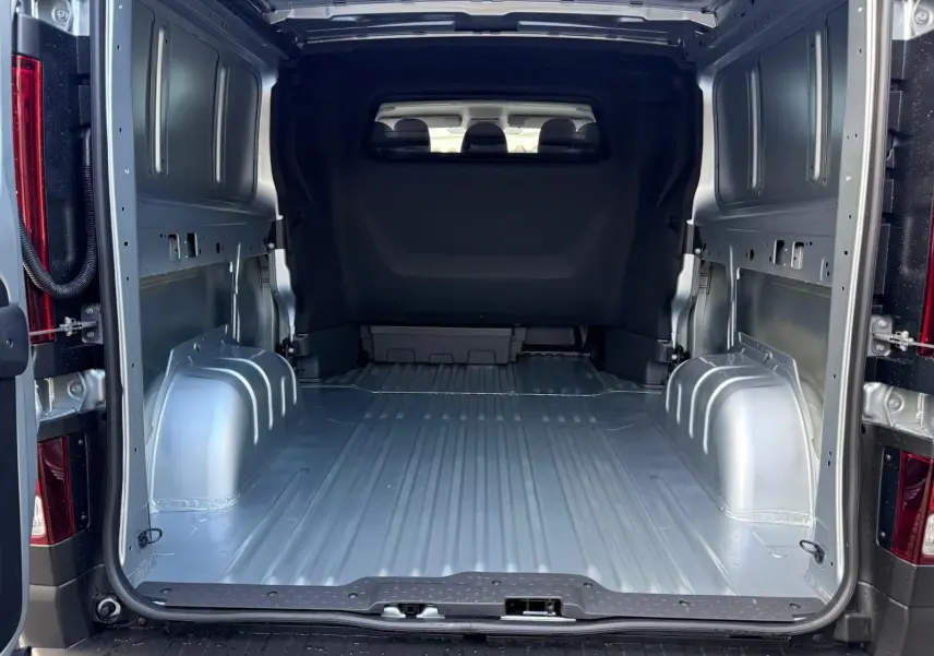 Vue 3/4 arrière droite d'un Renault Trafic cabine approfondie gris Highland avec vitres teintées et feux arrière verticaux.