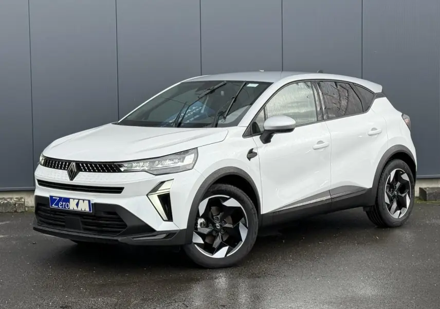 Renault Captur 2025 blanc nacré en 3/4 avant droit avec jantes noires et toit gris Highland visible.