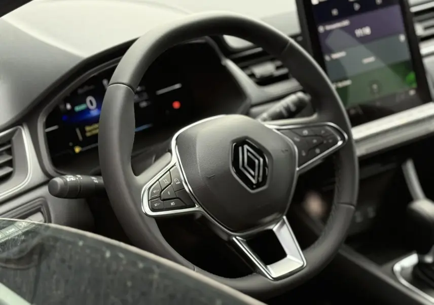 Volant noir avec logo Renault au centre, tableau de bord numérique et écran tactile dans l'habitacle du Renault Captur 2025.