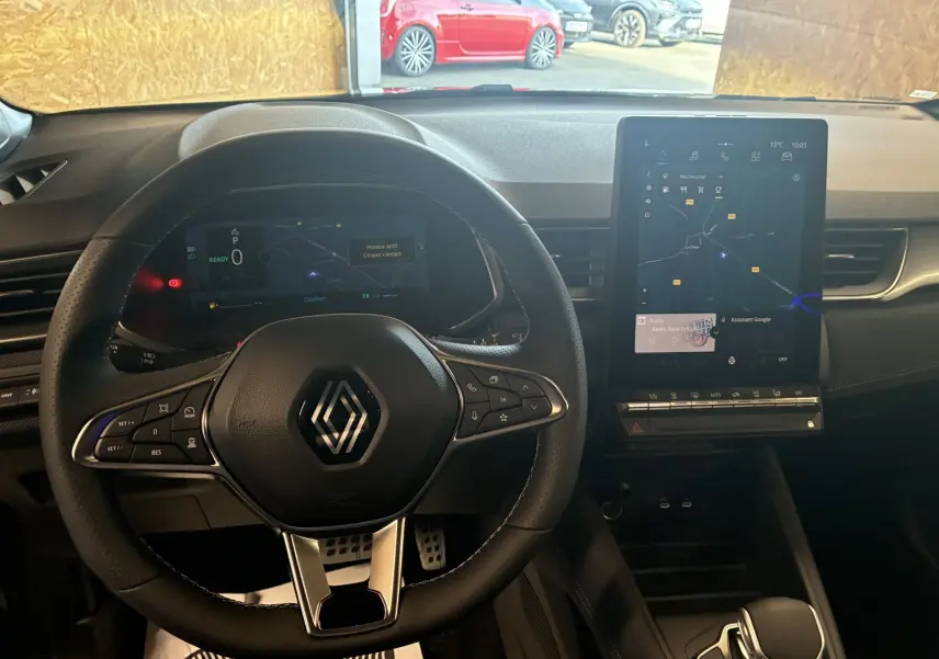 Vue intérieure du tableau de bord du Renault Captur E-Tech hybride 2025, volant noir avec écran tactile vertical central.