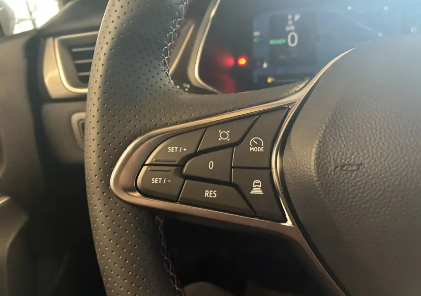 Gros plan sur les commandes au volant en cuir perforé noir du Renault Captur E-Tech 2025, avec tableau de bord numérique en arrière-plan.